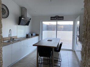 A modern kitchen with a wooden countertop, a sink, a kettle, and a toaster. There is a sign above the door that reads "BISTROT LES COPAINS D'ABORD".