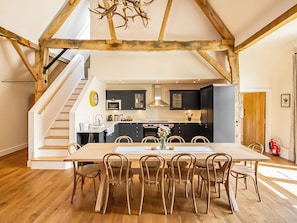 A modern kitchen with dark cabinets, a wooden dining table, and a staircase leading to an upper level. - Hatchers Barn - UK42080 (Shefford Woodlands Near Hungerford)