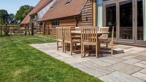 Ein Holzhaus mit gefliestem Patio, einem Esstisch mit Stühlen und einer großen Schiebeglastür.