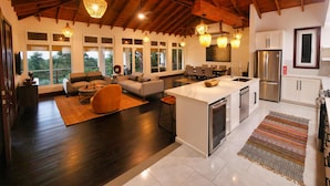 A spacious living area with a large island, dark wooden flooring, and a high ceiling with exposed beams. - Relax at this hillside retreat that overlooks the lush forest and the Caribbean. (West End)