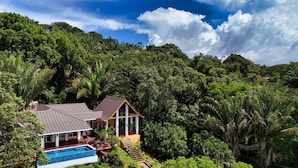 A house with a pool, surrounded by dense forest and a clear sky. - Relax at this hillside retreat that overlooks the lush forest and the Caribbean. (West End)
