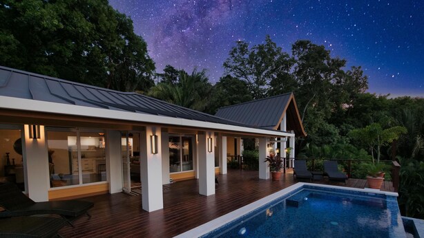 Una casa moderna con piscina, terraza de madera y vista al cielo nocturno.
