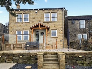 A stone house with a wooden front door, a small porch with a bench, and a stone staircase leading to the entrance. - Sykes Head Cottage - UK42147 (Oakworth)