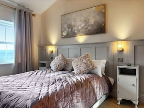 Een slaapkamer met een groot bed, twee nachtkastjes, een wandlamp en een raam met gordijnen.