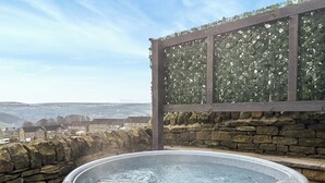 Un jacuzzi sur un balcon, avec un mur en pierre et une vue sur les maisons au loin.