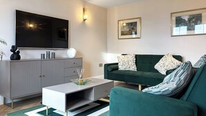 A modern living room with a flat-screen TV, grey cabinetry, a green sofa, and two framed pictures on the wall. - Sykes Head Cottage - UK42147 (Oakworth)