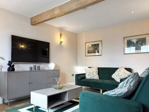 Una sala de estar moderna con un televisor de pantalla plana, muebles grises, un sofá verde y dos cuadros en la pared.