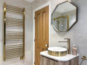 Une salle de bain avec un porte-serviettes doré, une porte en bois, un lavabo rond avec un robinet doré et un miroir avec un cadre doré.