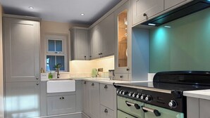 A modern kitchen with grey cabinets, a built-in oven, and a stainless steel range hood. - Sykes Head Cottage - UK42147 (Oakworth)