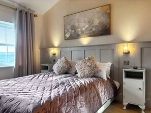 Une chambre à coucher avec un grand lit, deux tables de chevet, une commode, une lampe fixée au mur et une fenêtre avec des rideaux.