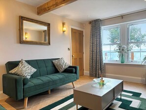A living room with a green sofa, a coffee table, a mirror, and a window with curtains. - Sykes Head Cottage - UK42147 (Oakworth)