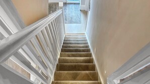 A carpeted staircase with white railings leading to a room with a view. - Sykes Head Cottage - UK42147 (Oakworth)