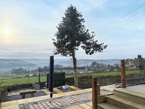 A patio area with a stone bench, a wooden post, and a view of a rural landscape with houses and fields.