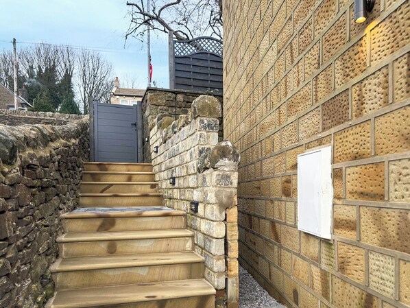 A stone staircase leading to a door, a brick wall with a security camera, and a metal gate in the background.