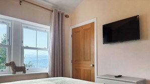 Une chambre à coucher avec un lit, une télévision, une fenêtre avec des rideaux et une vue sur l’extérieur.