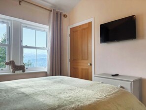 Un dormitorio con cama, televisión, ventana con cortinas y vistas al exterior.