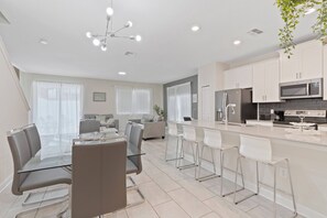 Una cocina moderna con gabinetes blancos, electrodomésticos de acero inoxidable y una isla central con taburetes de bar.