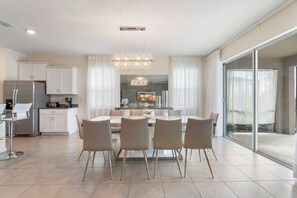 Una cocina moderna con armarios blancos, un refrigerador de acero inoxidable y una zona de comedor con una mesa de vidrio y cuatro sillas.