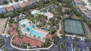 Vista aérea de un resort con piscina, cancha de tenis y zona de estacionamiento.