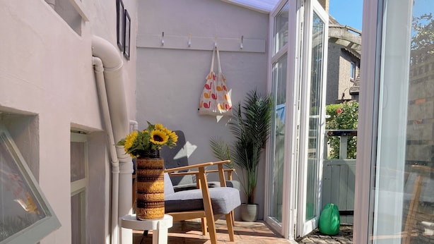 Un pati banyat per la llum del sol amb una cadira, un taulell, un vas amb girassols i una planta en test.