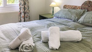 A neatly made bed with a floral-patterned bedspread, a green pillow, and a green nightstand with a lamp. - Siskin Lodge - UK39664 (Craobh Haven)