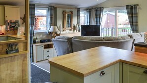 A compact, well-lit room with a kitchenette, a sofa, a TV, and a window with curtains.