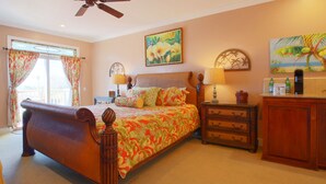 Une chambre à coucher avec un grand lit, une table de chevet, une commode et un ventilateur de plafond.