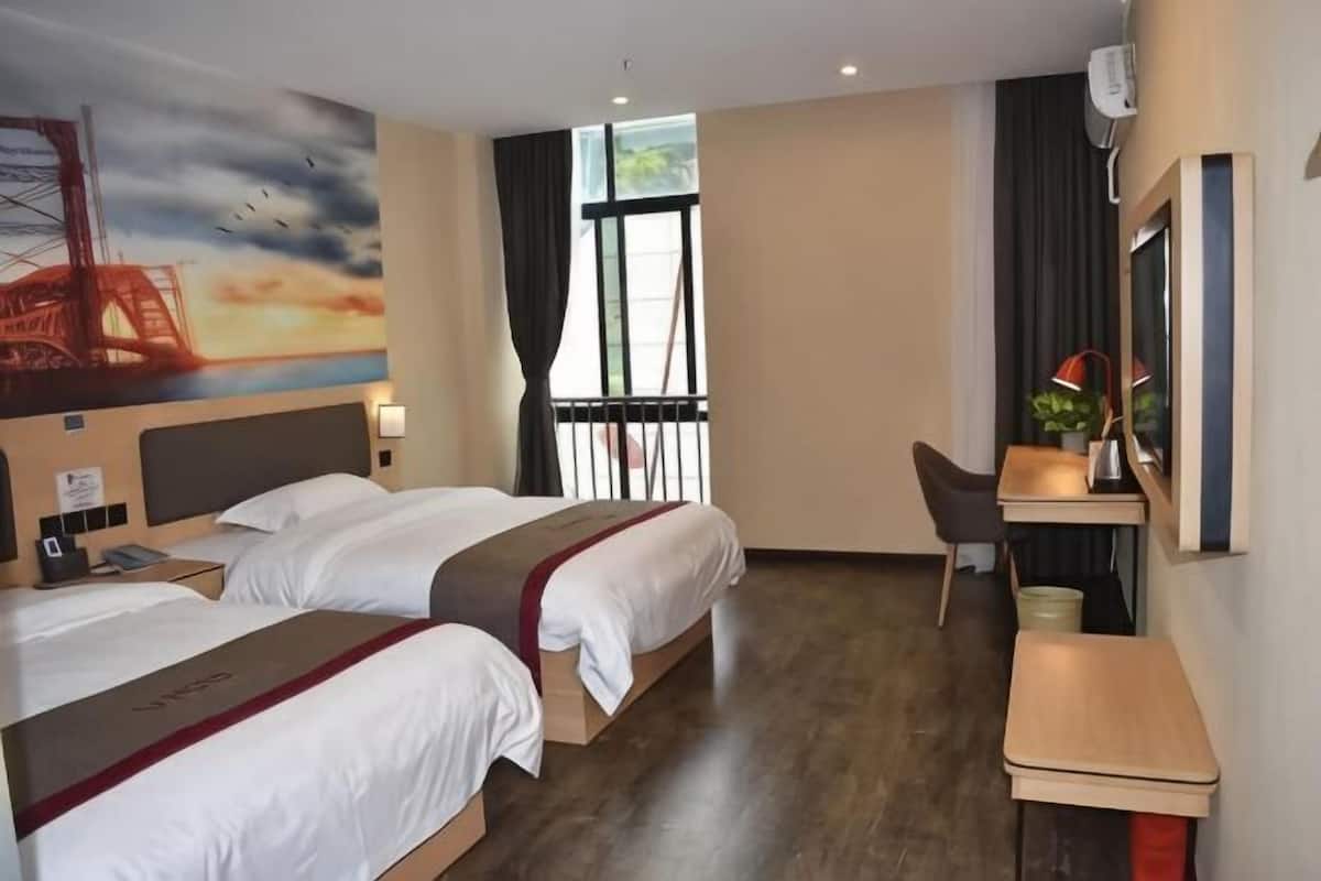 A hotel room with two beds, a desk, a chair, a window with curtains, a painting on the wall, and a plant on the desk.