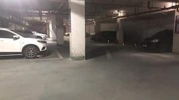 A parking garage with multiple cars parked under concrete pillars.