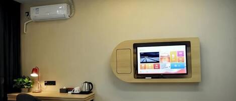 Habitación de hotel con escritorio, una silla, televisor de pantalla plana montado en la pared, una mesita y un equipo de aire acondicionado.