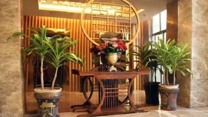 A reception area with a wooden reception desk, two potted plants, a decorative wall panel, and a large window. - Shankee Hotel (Xianyou Lizhong Pedestrian Street) (Xianyou)