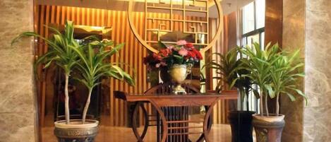 Een receptiezone met een houten receptiebalie, planten in potten en een decoratieve wand met een rond ontwerp.