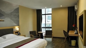 A hotel room with a bed, two chairs, a desk, a small table, a window with curtains, and a wall-mounted air conditioner. - Shankee Hotel (Xianyou Lizhong Pedestrian Street) (Xianyou)