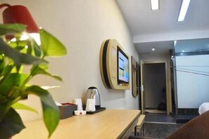 A hotel room with a wooden desk, a plant, a wall-mounted TV, and a door leading to another room. - Shankee Hotel (Xianyou Lizhong Pedestrian Street) (Xianyou)