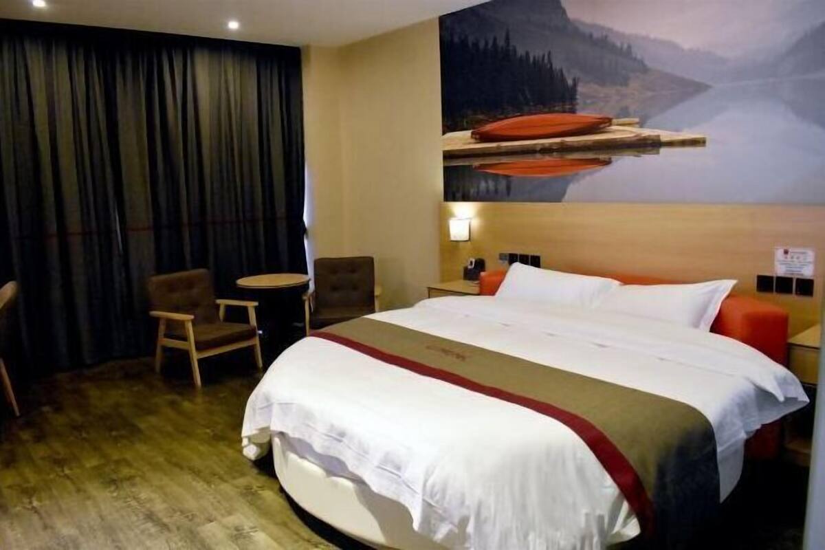 A hotel room with a large bed, a small table, a chair, and a painting of a lake scene.