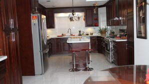 A modern kitchen with dark wood cabinets, stainless steel appliances, a central island with stools, and a chandelier. -  Large Comfy room w Private bath in gre (Richmond)