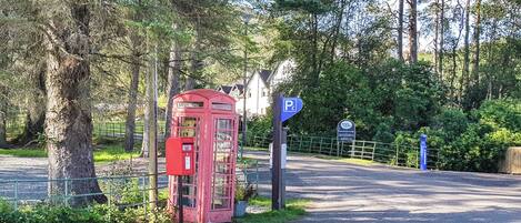 Une cabine téléphonique rouge et un panneau de signalisation de stationnement bleu, situés dans une zone boisée.