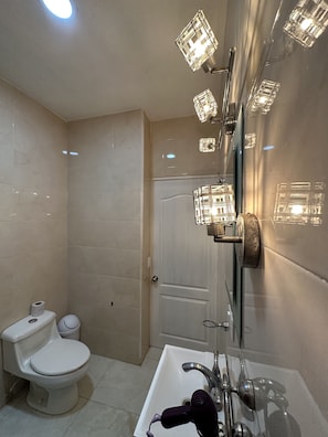 A modern bathroom with a white toilet, a sink with a handheld showerhead, and a glass-enclosed shower with multiple lights.