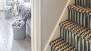 A staircase with a striped carpet, a grey upholstered bench, and a grey trash bin with a patterned cover.