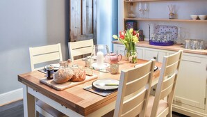 A dining table with a wooden top, surrounded by chairs, and a kitchen area with shelves and various kitchen items.