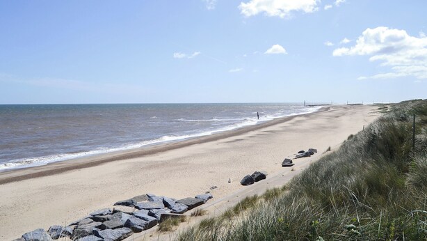 A sandy beach with a rocky breakwater and grassy dunes.