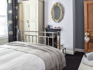 Quarto com uma cama, um guarda-roupa, um espelho e uma porta.