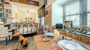 Um quarto acolhedor com cama, escada de madeira, área de jantar com mesa posta para dois e uma janela com persianas.