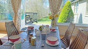 Un comedor con una mesa dispuesta para cuatro, sillas, un jarrón con flores y vistas al jardín.