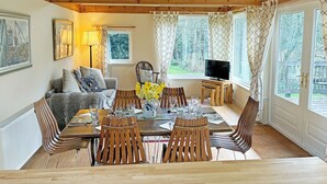 Un comedor con una mesa de madera, sillas, un televisor y una ventana con cortinas.