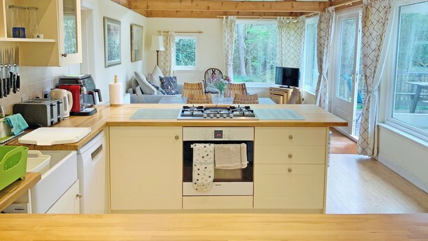 Una cocina con una isla central, vigas de madera, un comedor con sillas y ventanas grandes.