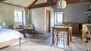 Una habitación amplia con una cama grande, una mesa de comedor de madera y sillas, una zona de cocina con un fregadero y armarios, y un techo con vigas de madera a la vista.
