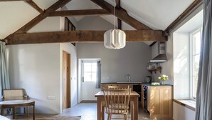 Una cocina amplia con vigas de madera, un comedor con mesa y sillas, y un gran ventanal con cortinas.