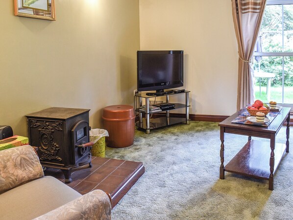 Una sala de estar con televisión, chimenea, sofá y una mesa con frutero.