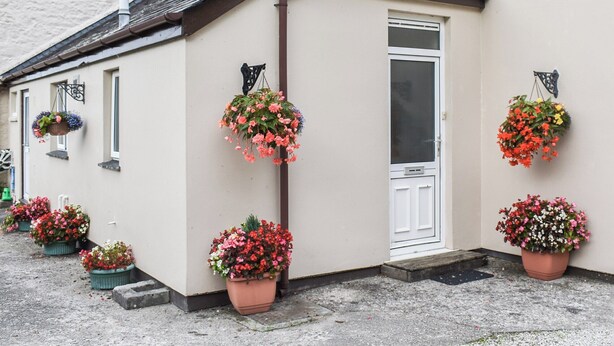 Un edificio con facciata bianca, un'entrata con una finestra e diversi vasi di fiori pensili.